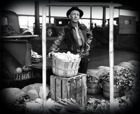 A man stands in front of a truck with a basket of produce