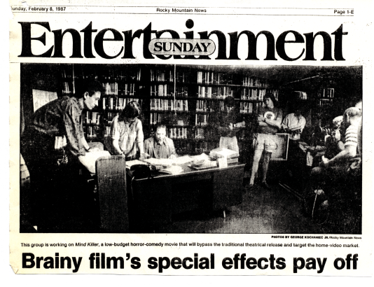 Clip from Rocky Mountain News article titled "Brainy film's special effects pay off." The image is six people standing in front of bookcases in Central Library basement with camera crew.