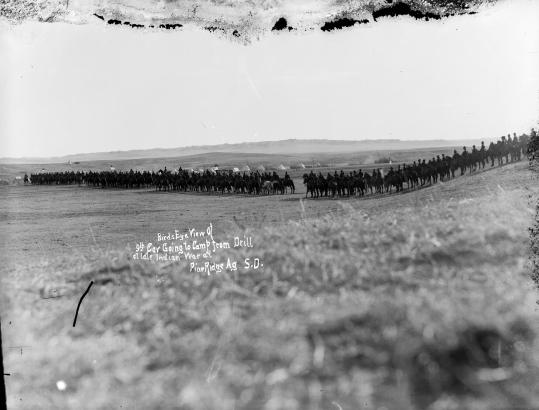 X-31372, Bird's eye view of the Ninth Cavalry of the U. S. Army, mounted Black buffalo soldiers ride in a long line back to their camp on the Native American Lakota Sioux, Pine Ridge Agency, South Dakota.