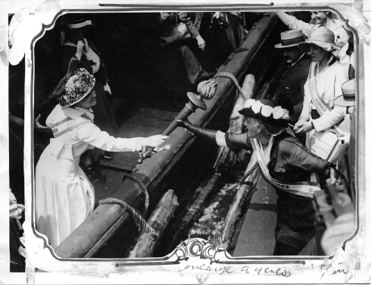 Passing the Torch August 11, 1915: A women's suffrage activist passes a torch from a boat to another woman.