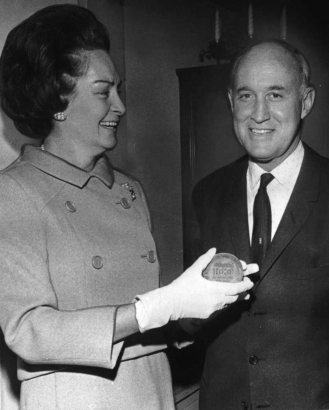 A man accepting an award from a woman in a stylish coat and gloves