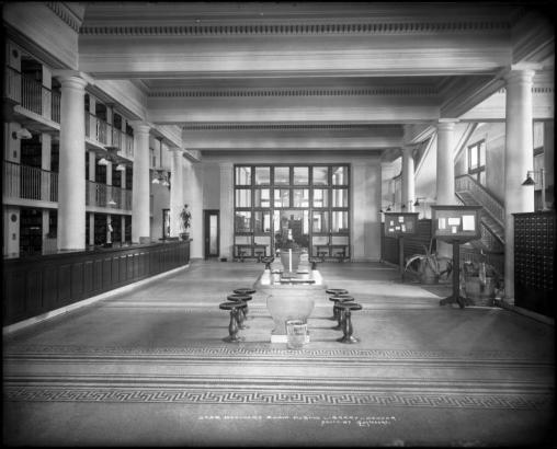 Interior view of the Delivery Room (Circulation Unit) at the main  (Civic Center) building of Denver Public Library, Denver, Colorado; at left is circulation counter, with three levels of shelving; at right are card catalogs, bulletin boards, and a stairway; at center are writing tables with stools.