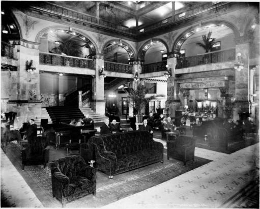 Interior view, lobby of the Brown Palace Hotel, located at 17th (Seventeenth) Street and Broadway in Denver, Colorado (completed in 1892); shows hotel guests on tufted sofas and chairs, potted palm at center of lobby, and staircase.