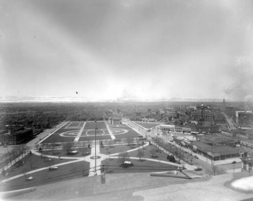 View west from dome of State Capitol Building over Civic Center, Denver, Colorado, shows the cruciform plan located between West Fourteenth Avenue and West Colfax. Landmarks include: Pioneer Monument, the Andrew Carnegie funded 1909 Denver Public Library, United States Mint, Arapahoe County Courthouse and the Daniels and Fisher Tower. Signs read: "Boss Rubber Co.," "Goodyear Tire & Rubber," "The Manualo," "The Baldwin Piano Co." and "Thurney Auto Co." Snowcovered Front Range shows in background.