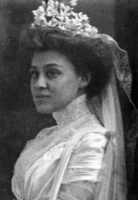 Wedding portrait of Louise Jeanette Bulkley wearing a high collared gown, flowered hat, lace, and organdy.