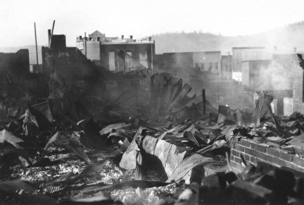 Destruction caused by second fire, April 29, 1896, Cripple Creek,  Colorado; shows rubble, debris, twisted sheet metal, brick foundation, two-story wood and brick commercial buildings with false fronts in background.