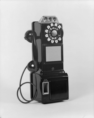 View of a pay telephone. The phone has a slot to deposit nickles, dimes, and quarters, a dial, and coin return.