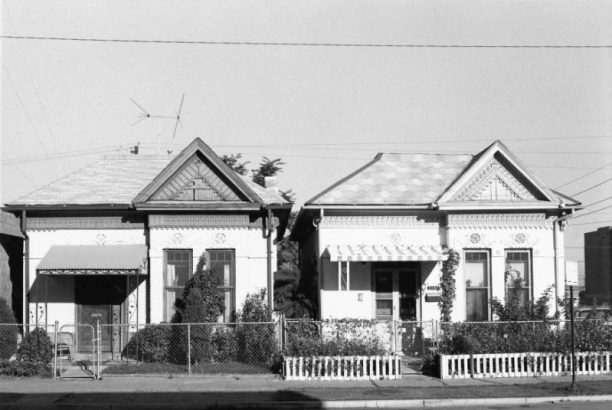 View of 2357 and 2361 Curtis Street in the Five Points neighborhood of Denver, Colorado.  Shows a pair of matching Queen Anne-style single family residences.  The one-story brick houses have a pedimented front gable window bay, scroll-sawn bargeboards, molded plaster rosettes, and decorative carved lintels.