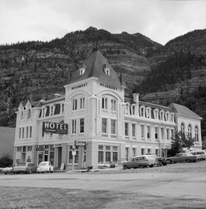 View of the Beaumont Hotel at the intersection of Fifth (5th) Avenue and Main (Third, 3rd) Street in Ouray, Ouray County Colorado. Designed by architect Mr. O. Bulow and built in 1886, the Gothic style brick and stone trim hotel has tower gables, a mansard roof, and a sign hanging perpendicular to front: "Hotel Beaumont, World Famous Historic Hotel," "Cocktails," and "Cafe."