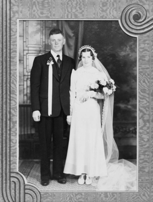 Wedding portrait of Mr. and Mrs. Grasmich, Ordway, Crowley County, Colorado. The bride wears a gown with veil and bouquet; the groom wears a suit with a ribboned boutonniere.