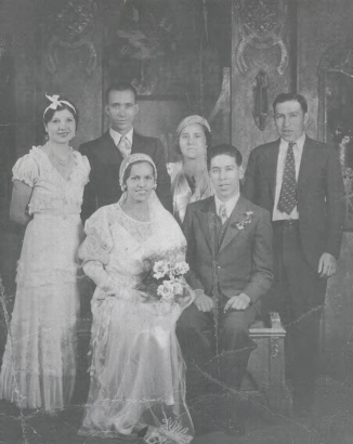 Studio portrait of the Edwardo Lopez and Ida Chavez Lopez wedding party, Denver, Colorado. They are identified (left to right) back row:  unknown woman, Manuel Moya, Racheal Chavez Moya, and Tony Lopez. Front row: Edwardo Lopez and his bride Ida Chavez Lopez. Ida wears a silk and lace wedding gown a lace veil and holds a bouquet of roses. Edwardo wears a suit and has a boutonniére. Racheal Chavez Moya wears a hat.