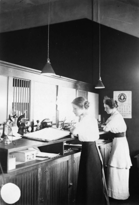 Two women work at ledgers while standing at a desk in a bank in Paonia, Colorado in Delta County.