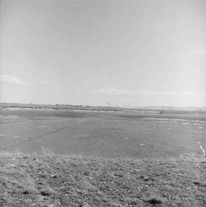 View of Rocky Flats in Golden, Jefferson County, Colorado (a Department of Energy site that manufactures plutonium triggers for nuclear weapons); shows buildings, fields, a water tower, and mountains.