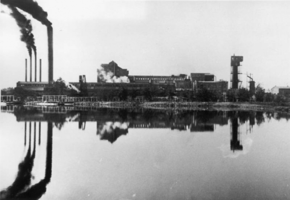 Reflection of the American Cystal Sugar Company factory, Rocky Ford, Otero County, Colorado, shows on foreground water. Smoke pours from stacks of the large sugar beet processing plant with hoppers, elevators and monitor roofed metal buildings.