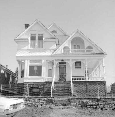 Exterior view of Charles N. and Josephine Miller's former residence, 127 West Carr, Cripple Creek, Colorado; This two-story Queen Anne style residence built in 1897 or 1898 has pitched roof porch with balustrades, and recessed and encircling porch; other characteristics include multi-gabled or triple gabled roof line, bay windows, tall stone foundation, bargeboard, scalloped shingling, and wire fence with gate around perimeter of yard.