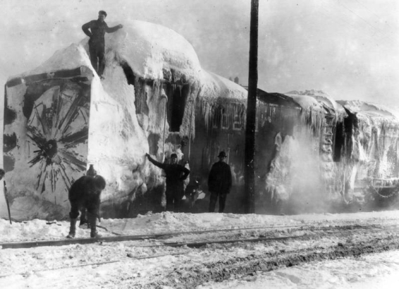 Four Denver & Salt Lake Railroad workers stand next to and on a snow-encrusted rotary plow that was involved in a train accident in Tabernash, Colorado in Grand County.  Steam rises off of the engine, and snow covers the ground around the tracks.