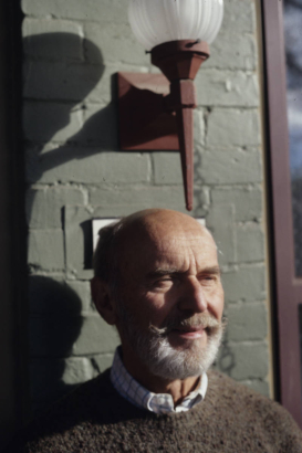 William Allen West, author and historic preservation advocate, poses on the porch of his home in the Curtis Park-Champa Street Historic District, in the Five Points neighborhood, Denver, Colorado. He is balding, has a beard and mustache and wears a sweater.