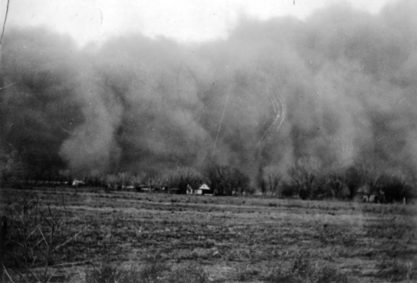 View of a huge dark cloud of dust possibly in Walsh, Baca County,  or Holly, Prowers County, southeastern Colorado. A house and line of trees  is barely visible. The devasting dust bowl carried top soil for miles.