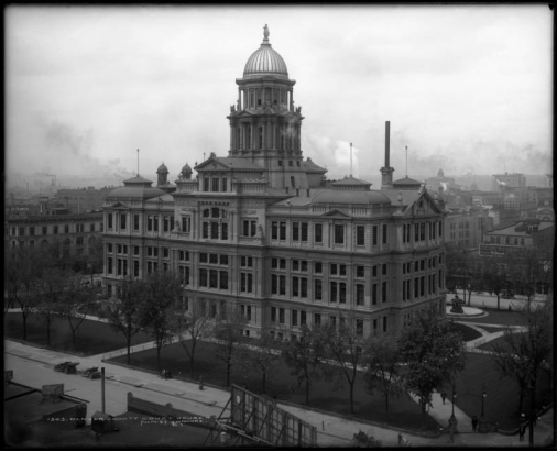 Bird's eye view of old Denver County Courthouse (also called Arapahoe County Courthouse), bounded by 15th & 16th Streets and Tremont & Court Places, Denver, Colorado; completed in 1883, demolished in 1933; well  or fountain behind courthouse, early automobiles parked at curb, billboards advertising "Lunch Room" and "Henry George nickel cigars".