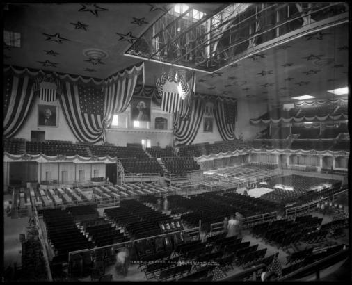 Interior view of City Auditorium on 15th (Fifteenth) between Curtis and Champa Streets, Denver, Colorado; soon after completion in 1908 being readied for Democratic National Convention in July, 1908; shows patriotic bunting and banners, large portrait of George Washington, rows of empty seats, and section of ceiling open to beams.
