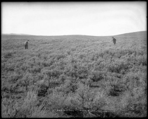 Two men about 30 feet apart hold a rope between them, probably near Craig, Colorado; early surveying for homestead boundaries, sage prairie.