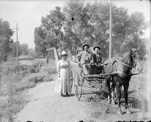 Outdoor portrait of people and a horse drawn buggy by the wood suspension bridge over Archer Canal in Denver, Colorado; the Alameda Avenue bridge is in the background.