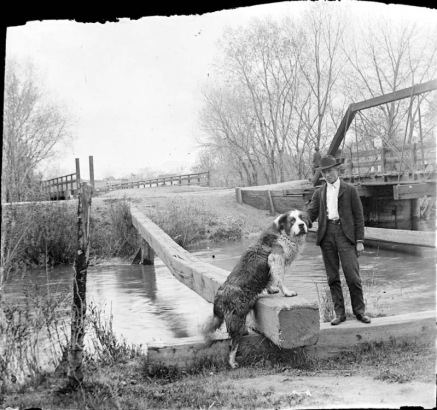 Portrait of a man with a Newfoundland dog by Archer Canal and the South Platte River bridge in Denver, Colorado.