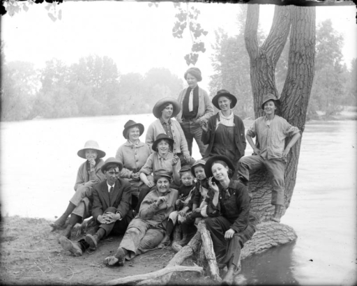 Outdoor portrait of a group of girls dressed as men and a man near the South Platte River in Denver, Colorado. The girls wear wide brimmed hats and hold pipes and cigarettes.