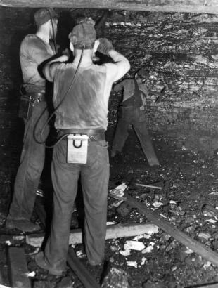 Miners work in a tunnel of the Columbine Mine near Erie (Weld County), Colorado. They wear hats and miner's lights.