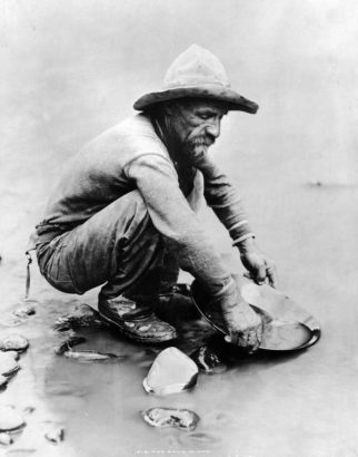 View of miner panning for gold in placer mining district of (possibly) Clear Creek west of Denver, Colorado