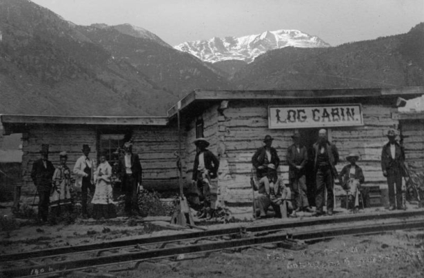 View of the Log Cabin, one of the first buildings built in Colorado Springs, El Paso County, Colorado. Governor Hunt built This cabin, when the Denver and Rio Grande railway arrived, in October 1871, it became the station restaurant. Identified figures, extreme left to right are: Governor Hunt, Mrs. Elisabeth Hunt McDowell (Hunt's daughter) Ed Eaton, Mrs. Helen McDowell Malhern, Major John H. McDowell (Hunt's son-in-law.) The McDowell's ran the restaurant.