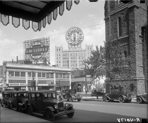 View, from Broadway and 18th (Eighteenth) Street, of the Continental Oil building at 17th (Seventeenth) Street and Glenarm Place in Denver, Colorado. Automobiles line the street near Trinity Methodist Church. Signs read: "Conoco Products", "Chevrolet", "Sightseeing Office", "City Trip $1.00", "Lookout Mtn. $2.50", "Rocky Mountain Cleaners And Tailors Phone Champa 3035-W", "Photo-engravers Artists Burke-McMillin Engraving Co. Illustrators Designers", "Marion Cafe", and "Au-to Shades".