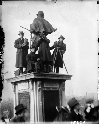 Photographers stand on the pedestal of the Soldier's Monument, which depicts a Union cavalryman, at the Colorado State Capitol Building in Denver, Colorado. They hold cameras and use cameras on tripods.