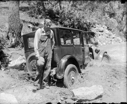 A man stands near his automobile that is stuck in a creek in Colorado.