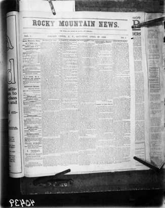 Shows a copy of the April 23, 1859 Rocky Mountain News, Vol.1, No.1, it's first edition. The paper is staged and clipped on a board for the photo. Under the banner "The Mines And Miners Of Nebraska;" headlines read: "The Opening Of Japan," "Alphabetical Conundrums," "The World Without A Sabbath," "Communications Received By The Nebraska Immigration Society," "Yankee Visit To Carlyle."
