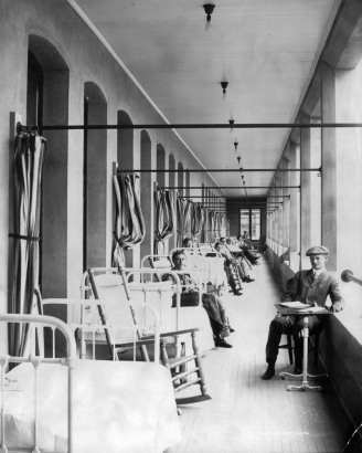 Tuberculosis patients in Denver, Colorado, enjoy fresh air on the balcony of the Agnes Memorial Sanatorium, built by Lawrences Phipps in 1903 and named for his mother Agnes McCall Phipps. The men sit in wicker rockers next to metal-framed beds separated by drawn curtains.