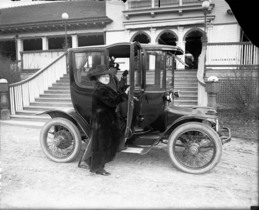 View of Addie Mellon and Harry Fisher Rhoads, parents of Harry M. Rhoads, with an electric automobile in front of City Park pavilion, Denver, Colorado.
