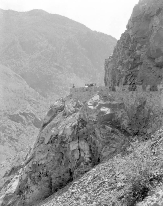 View of the Million Dollar Highway (State Highway 550), Ouray or San Juan County, Colorado; shows road grade, stone guardrails, a car, and a man.