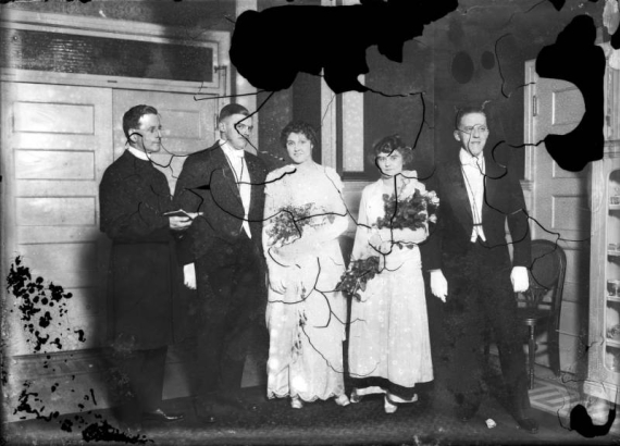 Portrait of brides, grooms, and a minister, probably in Denver, Colorado. The women hold flowers.