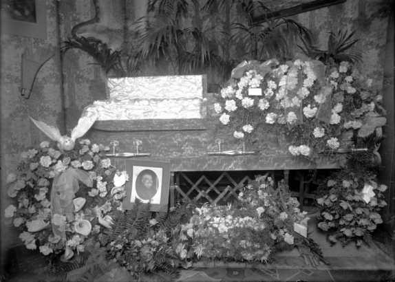 View of a coffin, flower arrangements, an artificial bird, a portrait of a man, and letters: "Father", probably in Denver, Colorado.