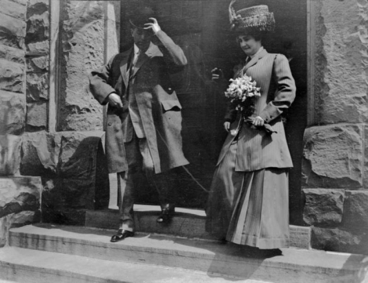 Charles and Hazel Gates pose on steps of Plymouth Congregational Church in Denver, Colorado after their wedding. Her outfit includes a straw hat and a bouquet of flowers.