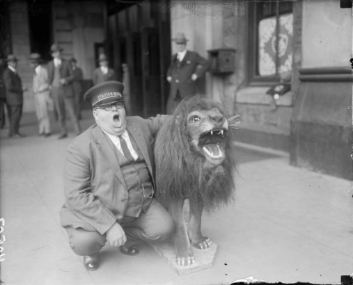 The station master at Union Station in Denver, Colorado stretches his mouth open in a "roar" to mock a fur covered statue of a roaring lion.