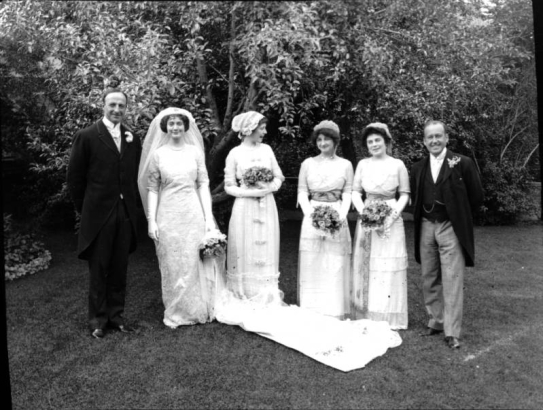 Portrait of a wedding group, in Denver, Colorado. The women hold flower bouquets, the bride wears a long train with her dress.