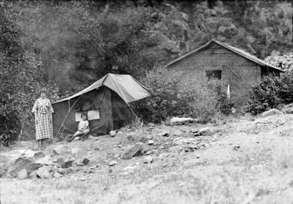 Sade and Mary Elizabeth Rhoads pose outside of a tent in Colorado. A tar papered shack is nearby.