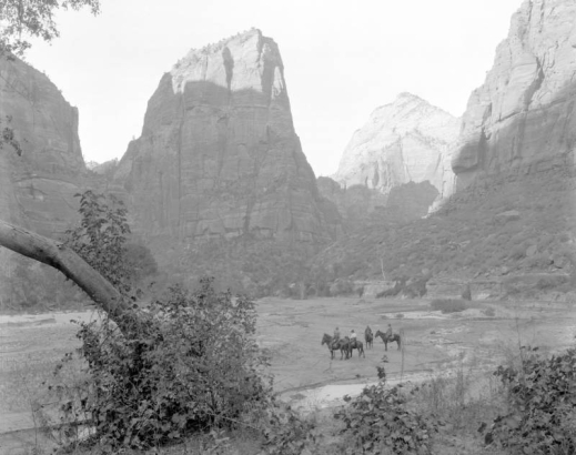 View of people riding horses on the valley floor between towering  cliffs at Zion National Park, Utah.
