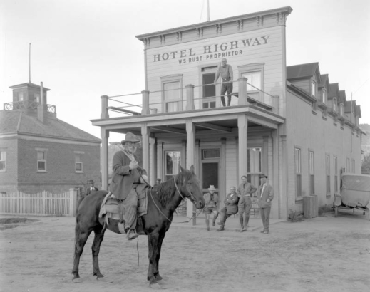 View of a hotel in Kanab, Kane County, Utah; shows a man on horseback with an axe, men on the porch or balcony of the frame structure, and lettering: "Hotel Highway W. S. Rust, Proprietor."