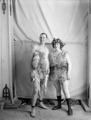 A man and woman pose in fur costumes; her brow is bound with a wreath.