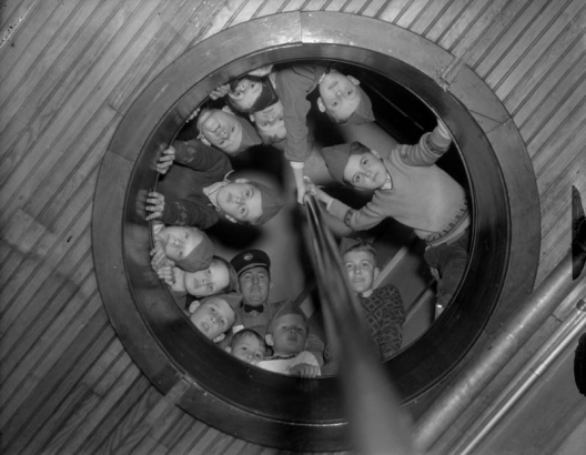Boy Scouts of America troop members and their troop leader look down a fire pole hole in a Denver, Colorado firehouse.