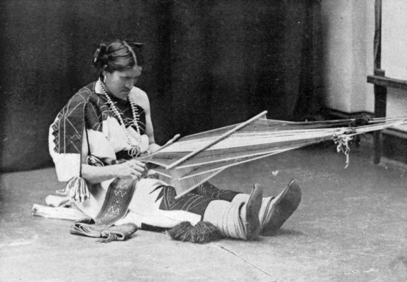 We'wha, a Native American (Zuni), sits and weaves a belt on a backstrap loom, Zuni Pueblo, New Mexico. We'wha is a berdache, a man who prefers women's work and adopts female dress; he is dressed as a woman and wears a woven manta, moccasins, and squash blossom necklace.