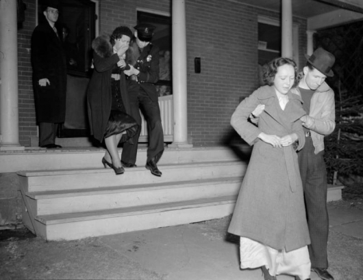 Two women are escorted from a home in Denver. One women is being led out by a police officer and the other woman is being led out by a man in plain clothes. They may be leaving the scene of a murder or suicide.